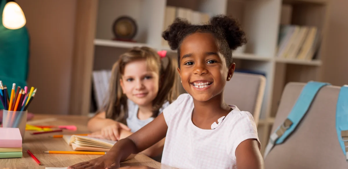 Two elementary students smiling at the camera while doing homework together